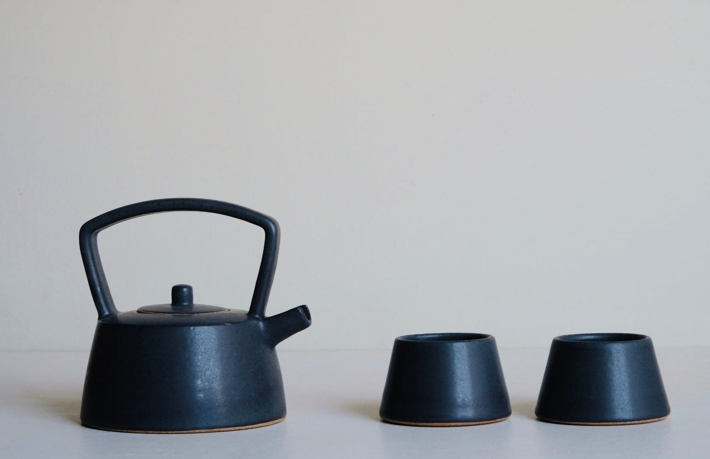 Black ceramic teapot and two matching cups on a light surface with a neutral background