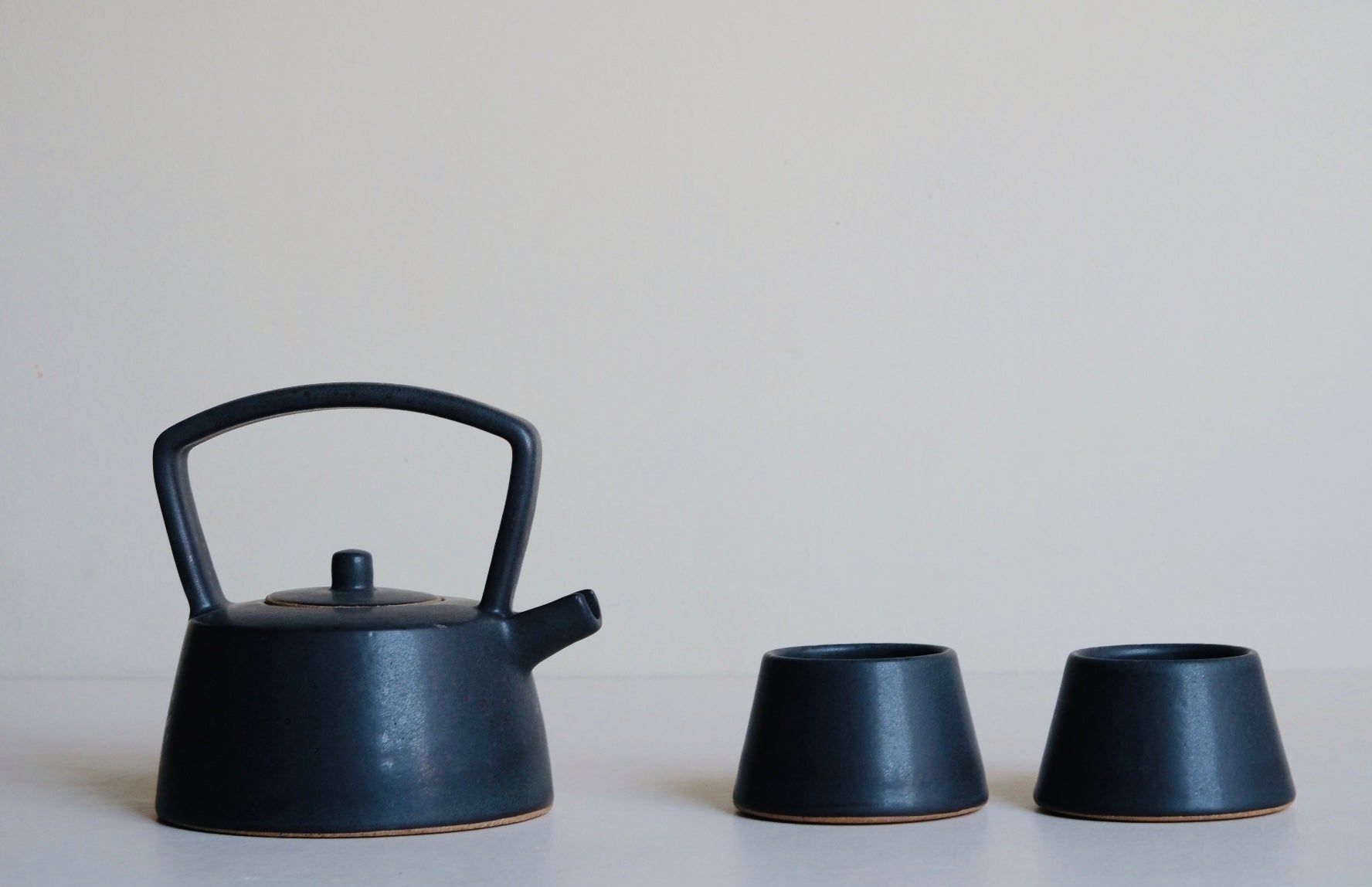 Black ceramic teapot and two matching cups on a light surface with a neutral background