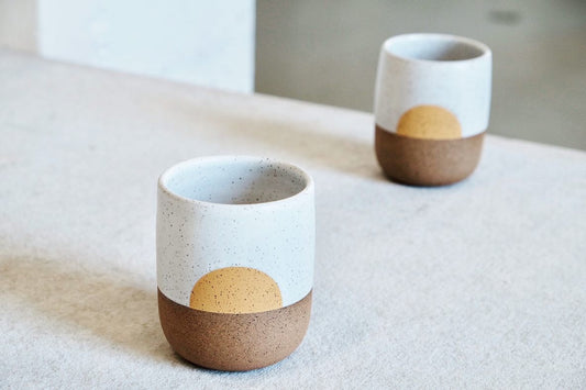 A handmade cup with a half-circle design in yellow.