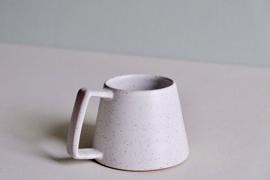 A speckled white mug with a wide bottom and large handle.