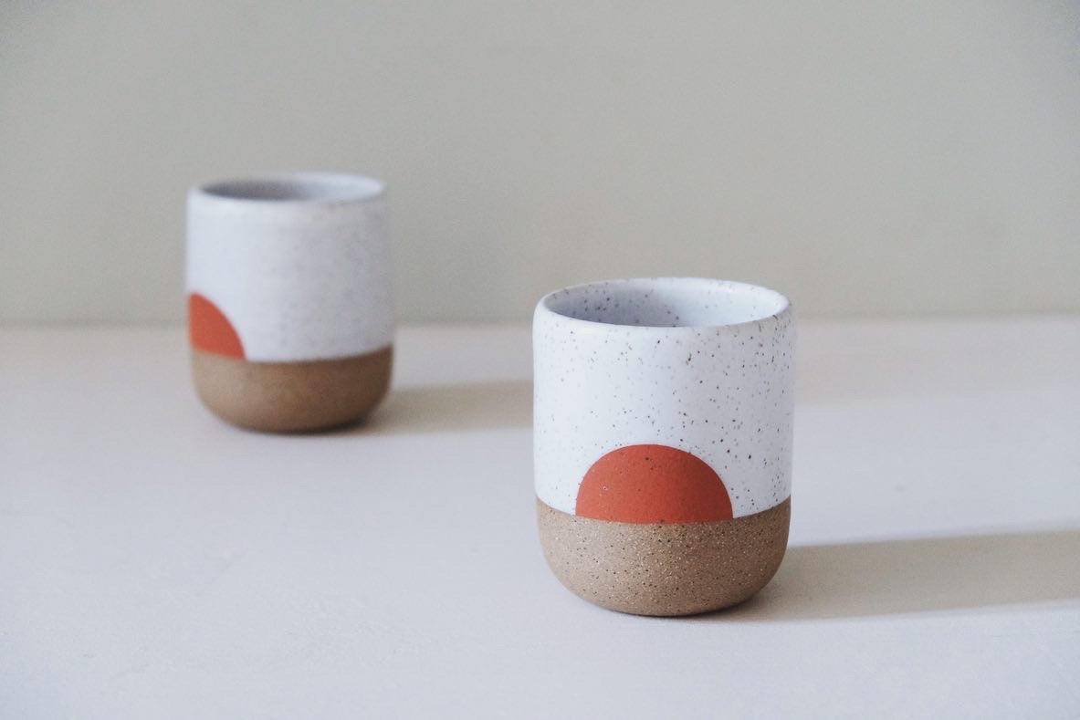 A handmade cup with a half-circle design in orange.