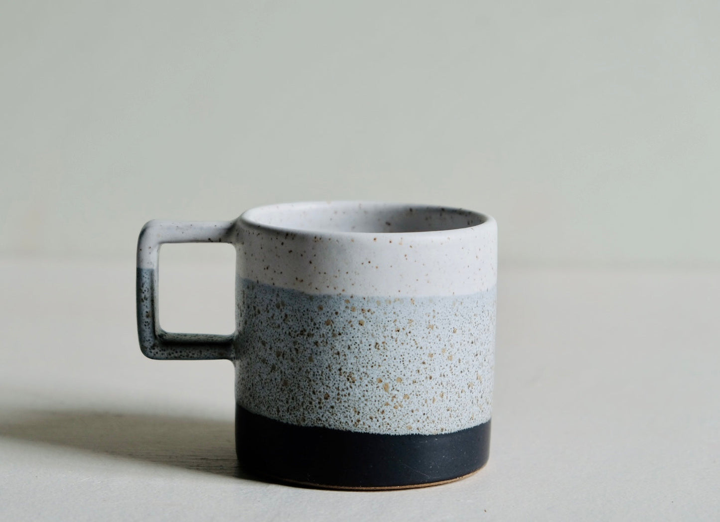 A handmade ceramic mug dipped in a luminous black, grey, and white speckled glaze
