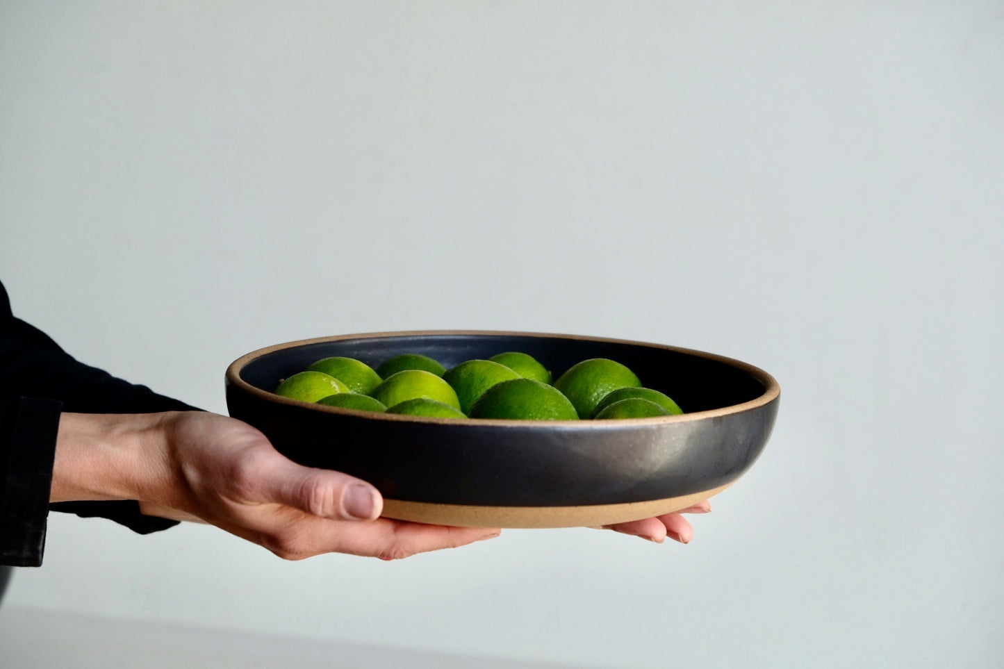 A medium serving dish that's dipped in black satin glaze with a raw rim and raw foot, handmade from speckled stoneware.