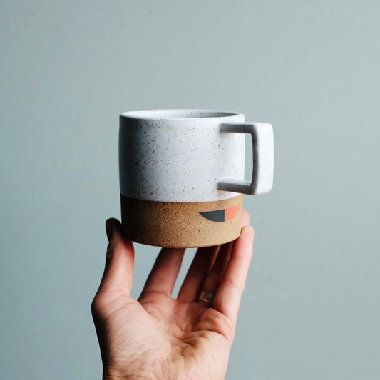 A handmade ceramic mug with  a square handle and a black and red gemoetric pattern applied as an undergalze