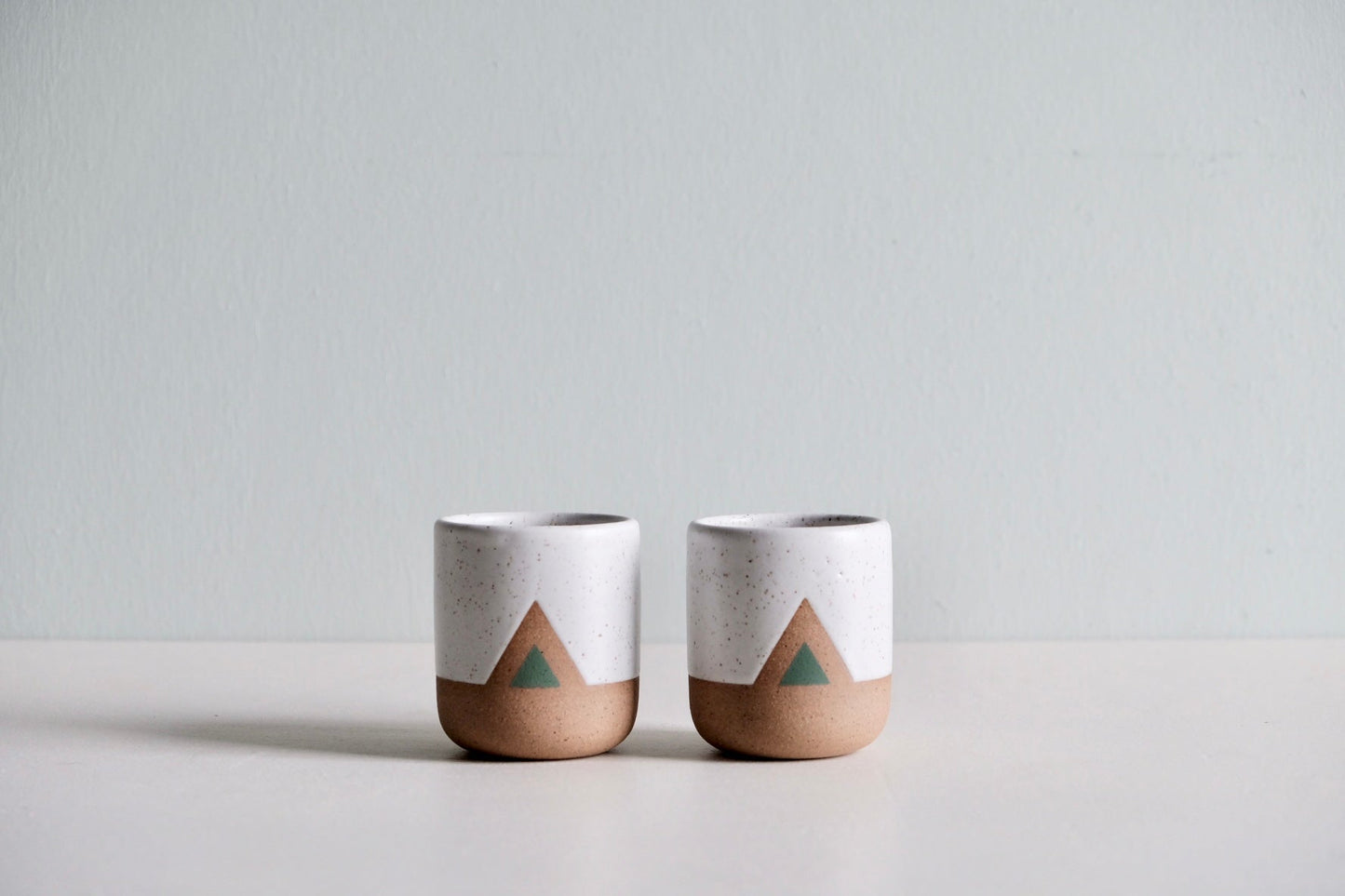 A handmade ceramic cup with a simple green triangular design.